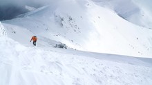  High Mountaineer Dressed Bright Orange Softshell Jacket Using A Trekking Poles Ascending The Snowy Mountain Summit. 4K UHD TV Active People Concept Footage.