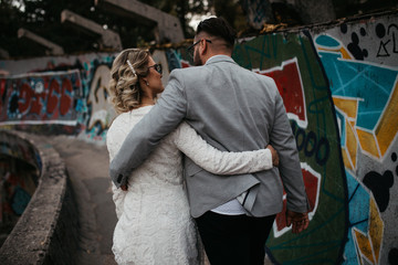 Wall Mural - Beautiful couple having a romantic moment on their weeding day, in mountains at sunset. Bride is in a white wedding dress with a bouquet of sunflowers in hand, groom in a suit. Happy hugging couple.