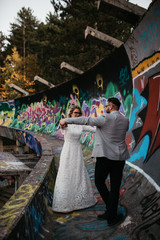 Wall Mural - Beautiful couple having a romantic moment on their weeding day, in mountains at sunset. Bride is in a white wedding dress with a bouquet of sunflowers in hand, groom in a suit. Happy hugging couple.