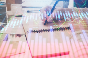 Poster - Hand taking notes in notepad. Forex chart holograms in front. Concept of research. Double exposure