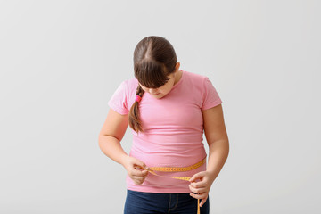 Poster - Overweight girl measuring her waist on light background