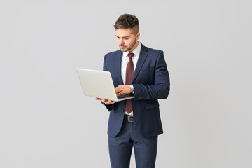 Wall Mural - Handsome businessman with laptop on light background