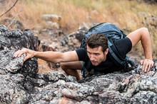 Mountain Climber Man Climbing To Mountain Peak. Handsome Confident Man Hiking With Backpack On The Rocky Mountain. Winning Life Achievement And Successful Business Goal Concept.