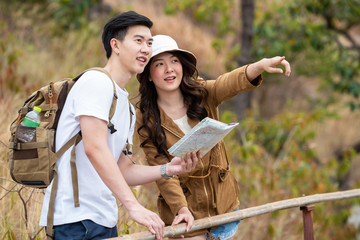 Happy young Asian couple man and beautiful woman with hiking together and looking the map for exploring the forest. Smiling boyfriend and girlfriend enjoy and having fun adventure in summer vacation