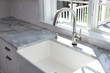 Modern kitchen sink and single handle brass faucet with soap dispenser, marble countertop and window to the garden.