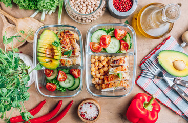 Healthy meal prep containers with chickpeas, chicken, tomatoes, cucumbers and avocados. Healthy lunch in glass containers on beige rustic background. Zero waste concept. Selective focus.