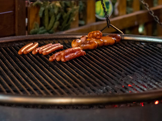 Appetizing delicious sausages lie on the grill of a roasting pan in the dark. From underneath the grill, hot coals burn. Outdoor festive refreshments in the city.