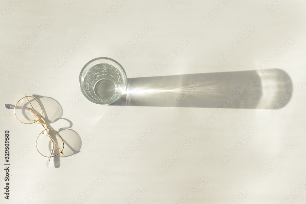 Glass of water with eyeglasses on white background
