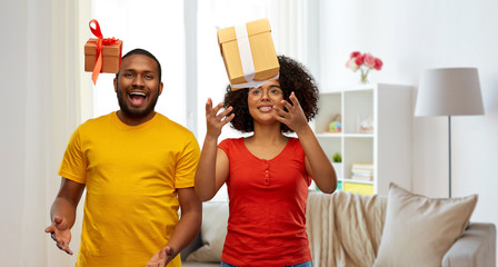 Wall Mural - holiday, greeting and people concept - happy smiling african american couple throwing gift boxes over home background