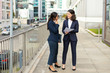© Mangostar - Professional businesswomen discussing papers. Full length view of female colleagues in formal wear standing on street and discussing work. Paperwork concept