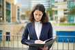 © Mangostar - Serious businesswoman reading papers. Front view of concentrated middle aged businesswoman in formal wear holding folder with documents on street. Paperwork concept