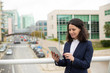 © Mangostar - Smiling woman using tablet computer. Content middle aged businesswoman using digital tablet while standing on urban city street. Wireless technology concept