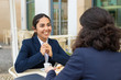 © Mangostar - Smiling businesswomen talking and drinking coffee. Professional female coworkers in formal wear sitting at table and drinking coffee together in outdoor cafe. Coffee time concept