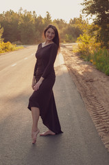 happy free girl barefoot on the pavement in a stylish long dress dancing at sunset