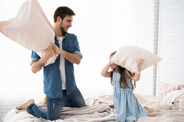 Wall Mural - happy father and daughter playing pillow fight in bed at morning