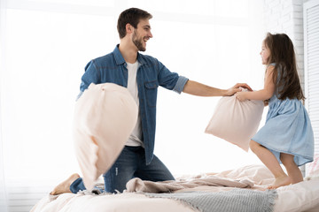 Wall Mural - happy father and daughter playing pillow fight in bed at morning