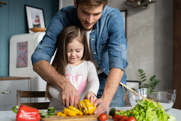 Handsome man and his little cute daughter are cooking on kitchen. Making salad. Healthy lifestyle concept.