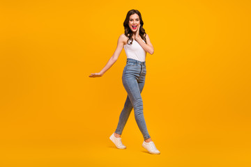 Poster - Full body profile photo of attractive cheerful lady good mood walk street arm on cheek wear white tank-top jeans footwear isolated bright yellow color background