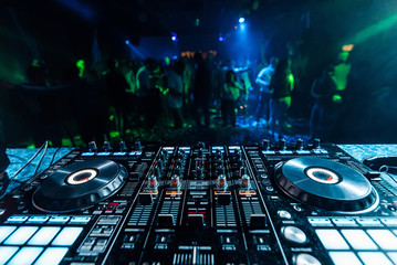 professional music DJ mixer in a booth in a nightclub on the background of blurred silhouettes of dancing people