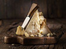Piece Of Parmesan Cheese And Cheese Knife On The Wooden Board. Dark Background.