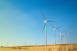canvas print picture - Windmills wind turbines farm power generators against landscape against blue sky in beautiful nature landscape for production of renewable green energy. Friendly industry to environment.