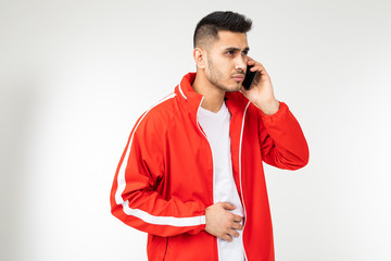 brunette stylish man in a red sports jacket is talking on a smartphone on a white empty background