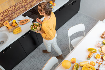 Wall Mural - Young and cheerful woman cooking with a variety of fresh vegetables and fruitson the kitchen at home. Eating of fresh healthy food concept