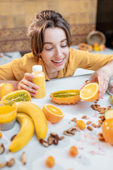 Wall Mural - Portrait of a young and joyful woman holding bottle of juice at the table full of healthy raw vegetables and fruits. Concept of vegetarianism, detox, healthy eating and wellness