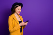 © deagreez - Turned photo of positive cheerful girl blogger use her smartphone read social network news follow posts enjoy wear yellow blazer bright headwear isolated over violet color background