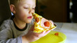Dziecko zjada kawałek pizzy. Chłopiec trzyma pizzę i patrzy na nią, jest głodny i zjada posiłek ze smakiem. Dzieci niejadki zastanawiają się nad tym czy zjeść.