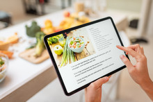 Woman Looking On The Digital Recipe, Using Touchscreen Tablet While Cooking Healthy Meal On The Kitchen At Home, Close-up View On The Screen