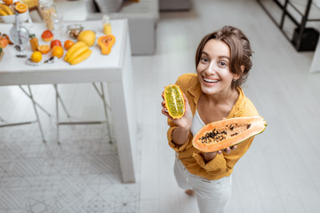 Portrait of a young and cheerful woman with exotic fruits at home. Concept of wellbeing, healthy food and homeliness