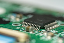 Macro Photo With Narrow Depth Of Field Of An Electronic Circuit With A Microcontroller & Components In Frame On Green Electronic Board.