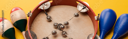 Fotografía Close up view of tambourine near colorful and blue maracas on yellow background,