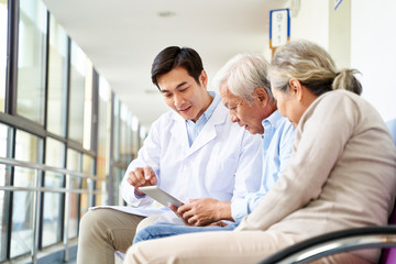 Wall Mural - young asian doctor talking to senior couple patients in hospital hallway