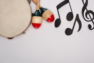 Top view of wooden maracas near tambourine and paper cut music notes on white background