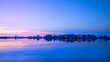 still lake and houses with light on at sunset; the sky at sunset and waterscape in township