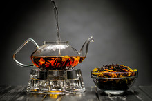 Horizontal Photo Of The Tea Set On A Black Background. Glass Transparent Teapot And Cup. Black Leaf Tea.