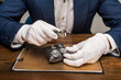 Cropped view of jewelry appraiser holding magnifying glass and earnings on board on table isolated on grey