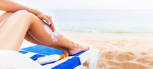 Young Woman Is Having Rest On The Sunbed At The Beach And Protects Her Skin Applying Sunblock On Her Leg