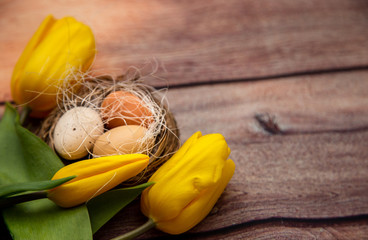 Easter eggs in a basket with yellow tulips on a brown wooden background.