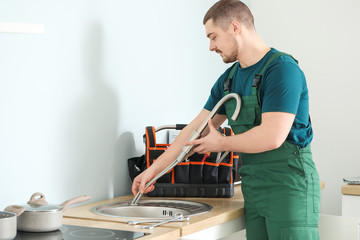 Poster - Handsome plumber repairing sink in kitchen