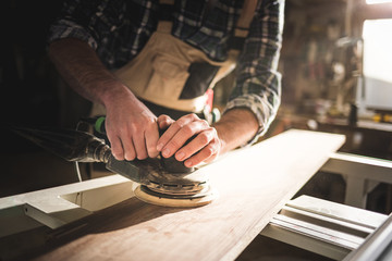 Close up of sanding a wood with orbital sander at workshop