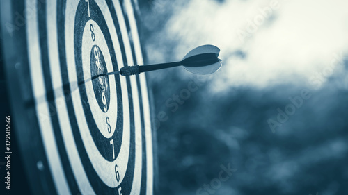Cuadros en Lienzo Businessman standing lookup red dart arrow hitting target centre dartboard on sunset background