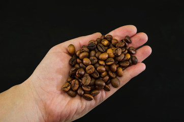 roasted coffee beans in a hand on a black background. View from above.