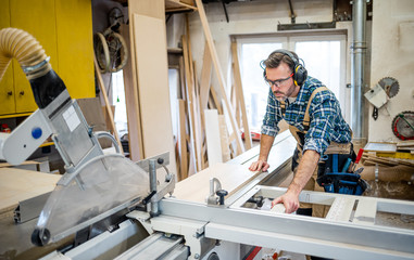 Carpenter using circular saw to cut a large wooden board at carpentry workshop