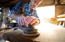 Carpenter At Workshop Polishes Wooden Board With A Electric Orbital Sander