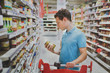 © Song_about_summer - buying food in supermarket grocery store, man customer reading ingredients on the jar of conserve olives