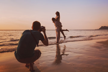 Wall Mural - wedding portrait photographer taking photos of honeymoon couple on the beach at sunset, professional