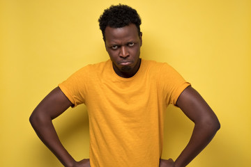 African american displeased, angry, grumpy and pissed off male looking and frowning at camera, pursing lips, having bad mood, feeling dissatisfied. Studio shot on yellow wall